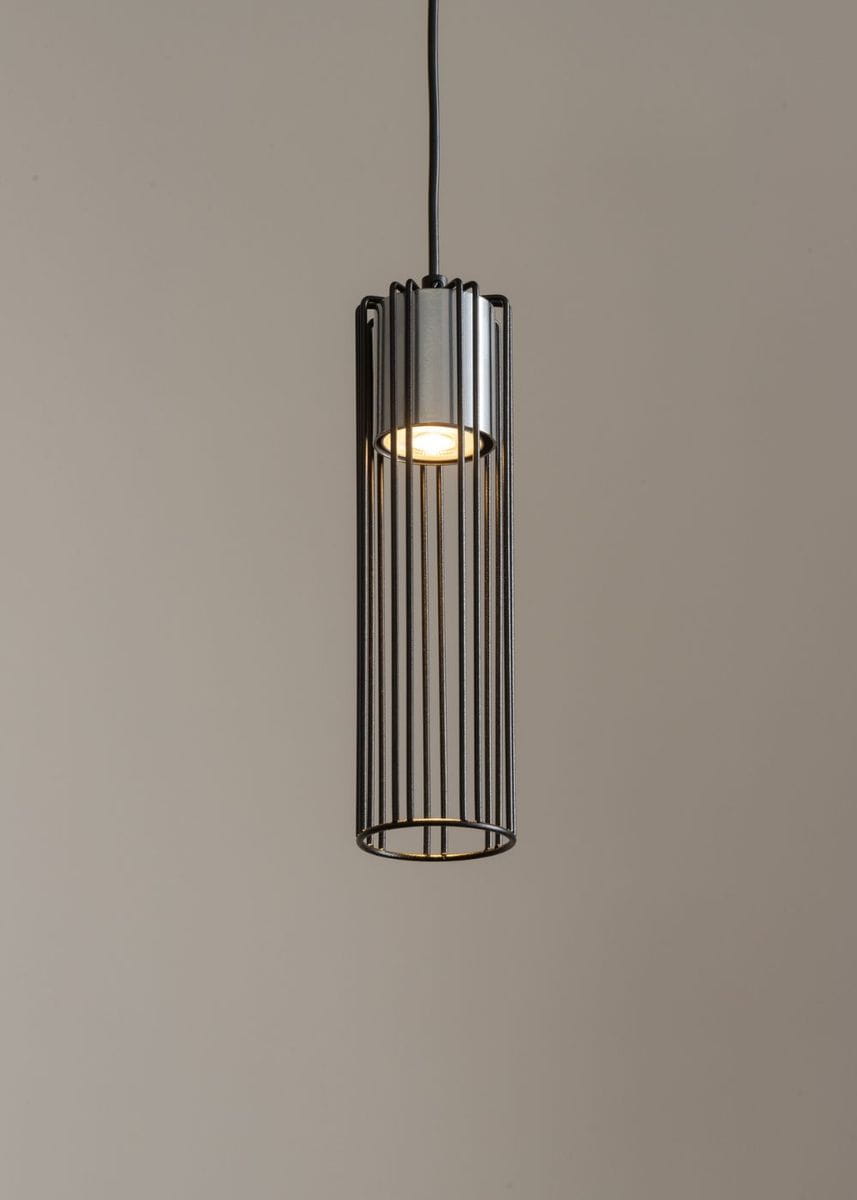 Lampa wisząca Fobia 1-punktowa w kolorze czarnym i srebrnym, o cylindrycznym kształcie z metalowymi szczelinami. Zawieszona na czarnym przewodzie, ukazuje źródło światła w górnej części. Tło w neutralnym odcieniu.