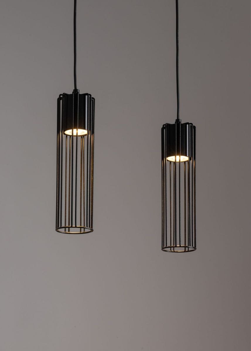 Czarna lampa wisząca Fobia 2-punktowa z metalowymi, szczelinowymi kloszami w kształcie cylindrów. Zawieszona na cienkich kablach, emitująca ciepłe światło. Produkt umieszczony na jednolitym tle, w pozycji wiszącej.