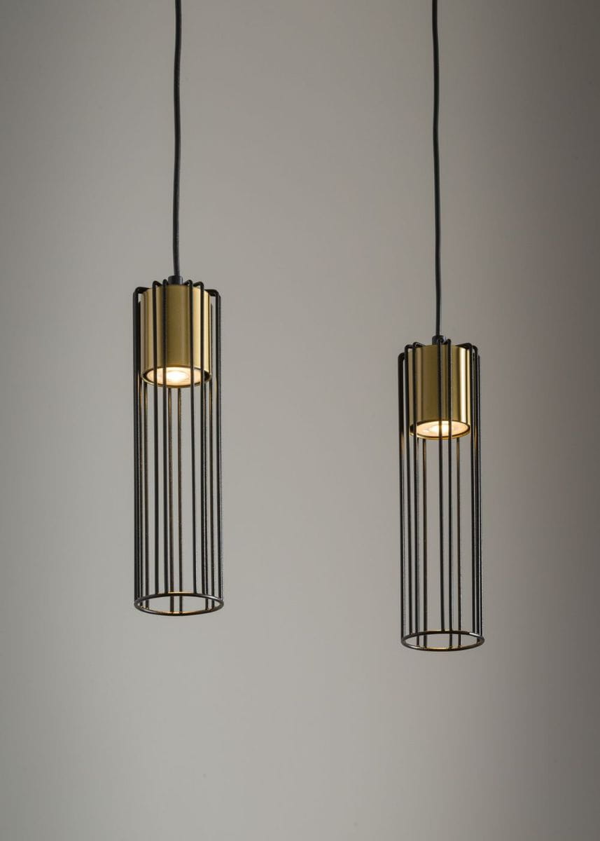 Lampa wisząca Fobia 2-punktowa w kolorze czarnym i złotym. Dwa cylindryczne klosze z metalowymi prętami, zawieszone na czarnych przewodach. Klosze mają złote detale u góry, emitując światło z wnętrza. Tło w jednolitym, jasnym kolorze.