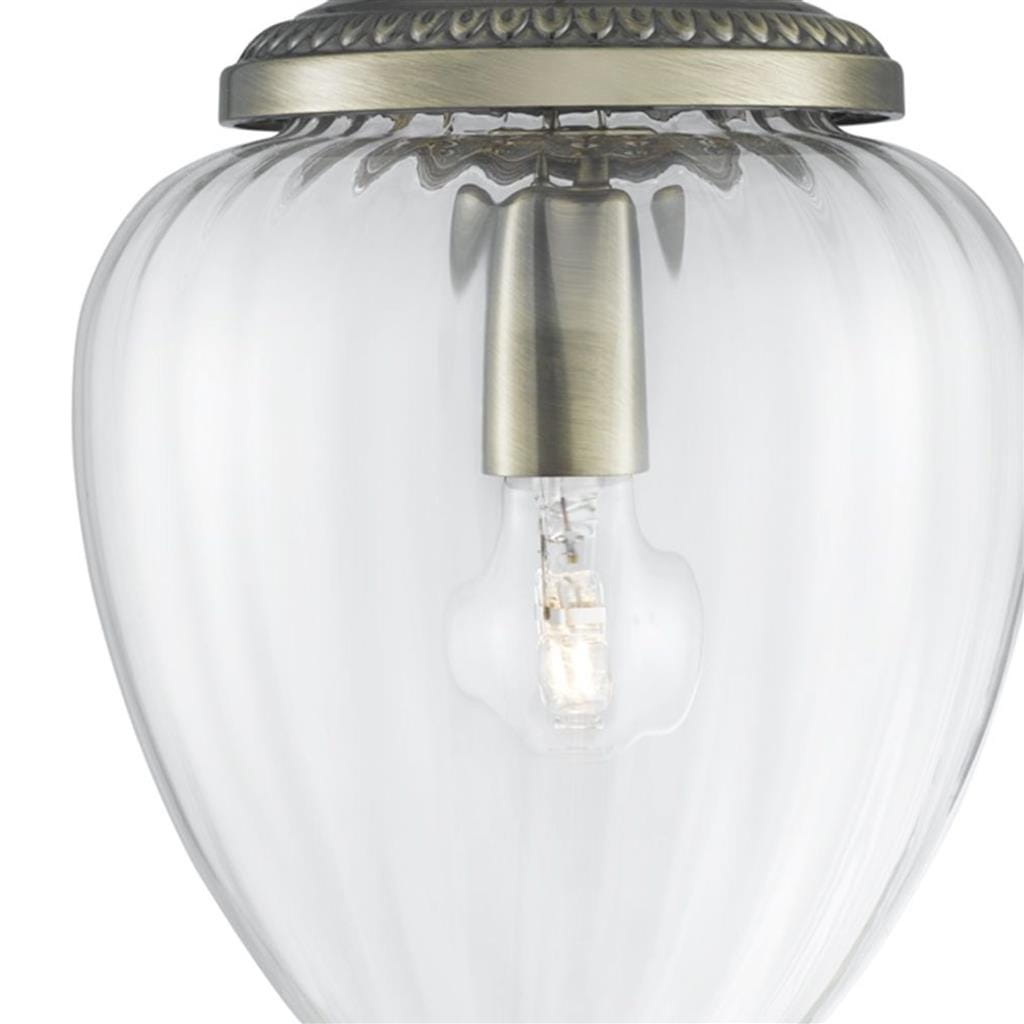 Lampa wisząca Moscow 1-punktowa w antycznym mosiądzu. Szklany klosz w kształcie owalnym, przezroczysty, z widoczną żarówką wewnątrz. Elementy metalowe w kolorze antycznego mosiądzu, zdobione na górze. Ujęcie z dołu, ukazujące detale konstrukcji.
