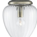 Lampa wisząca Moscow 1-punktowa w antycznym mosiądzu. Szklany klosz w kształcie owalnym, przezroczysty, z widoczną żarówką wewnątrz. Elementy metalowe w kolorze antycznego mosiądzu, zdobione na górze. Ujęcie z dołu, ukazujące detale konstrukcji.