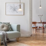 Lampa wisząca Cameroon 1-punktowa w kolorze antycznego mosiądzu, z kloszem w kształcie stożka, zawieszona w jasnym wnętrzu. W tle widoczny zielony sofa z poduszką oraz stół z krzesłami, na podłodze parkiet w jodełkę.