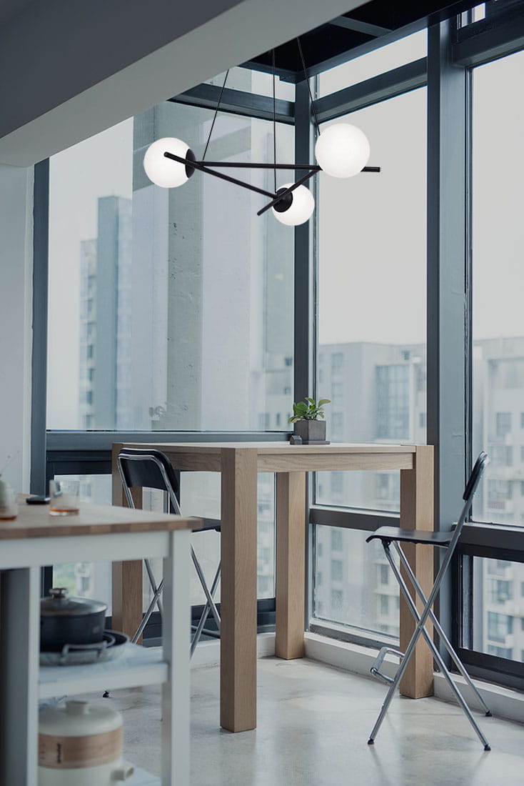 Arton lampa wisząca 3-punktowa w kolorze czarnym, z trzema okrągłymi kloszami w białym kolorze. Zawieszona na cienkich linkach, w nowoczesnym stylu. Widoczna w aranżacji kuchennej, nad drewnianym stołem i metalowymi krzesłami.