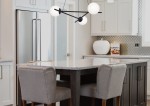 Lampa wisząca Arton 3-punktowa w kolorze czarnym z trzema białymi kloszami, zawieszona nad kuchennym wyspą. Kąt ujęcia z boku, ukazujący nowoczesny design i minimalistyczny styl. Tło jasne, kuchenne z elementami w odcieniach szarości i bieli.