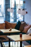 Lampa wisząca Arton 2-punktowa w kolorze czarnym z białymi, okrągłymi kloszami zawieszona w nowoczesnej aranżacji. Widoczna na zdjęciu w kontekście kawiarni z drewnianymi stolikami i miękkimi poduszkami na kanapie.