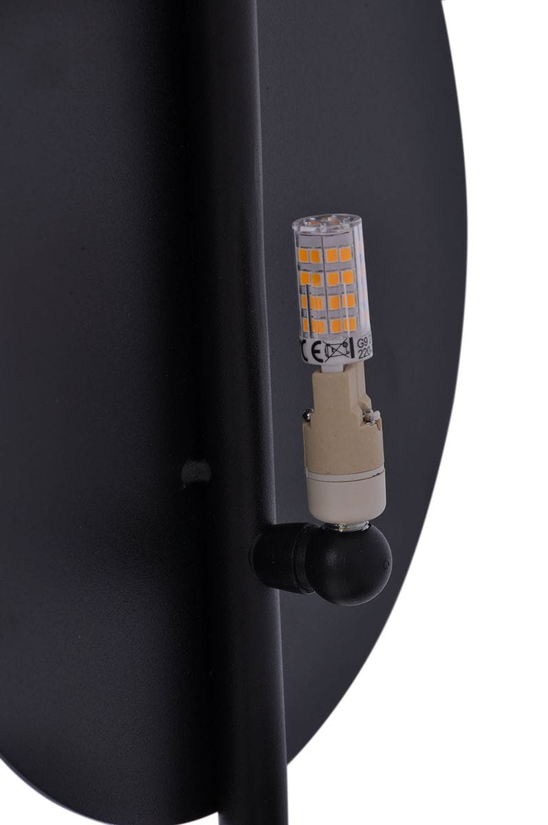 Czarny kinkiet 1-punktowy Rega K-4637, z okrągłą podstawą i widoczną żarówką LED G9. Produkt zamontowany na ścianie, z wykończeniem matowym. Widać detale mocowania oraz strukturę materiału. Tło jednolite, ciemne.