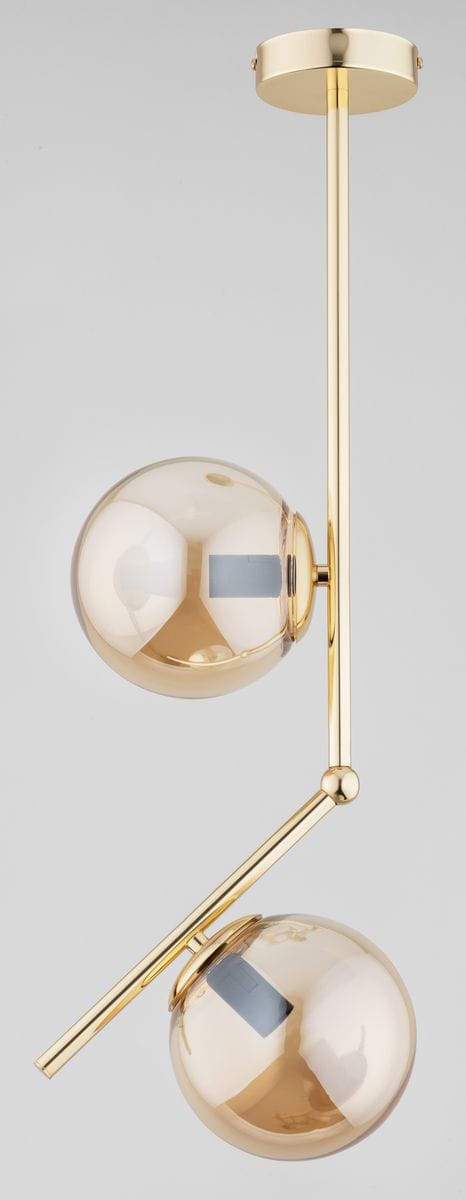 Lampa wisząca Liberty 2-punktowa w kolorze złotym, z dwiema kulistymi kloszami z przezroczystego szkła. Ułożona w pionie, z metalowym, błyszczącym wykończeniem oraz nachyloną rurką, zawieszona na okrągłym stelażu. Tło jasne, neutralne.