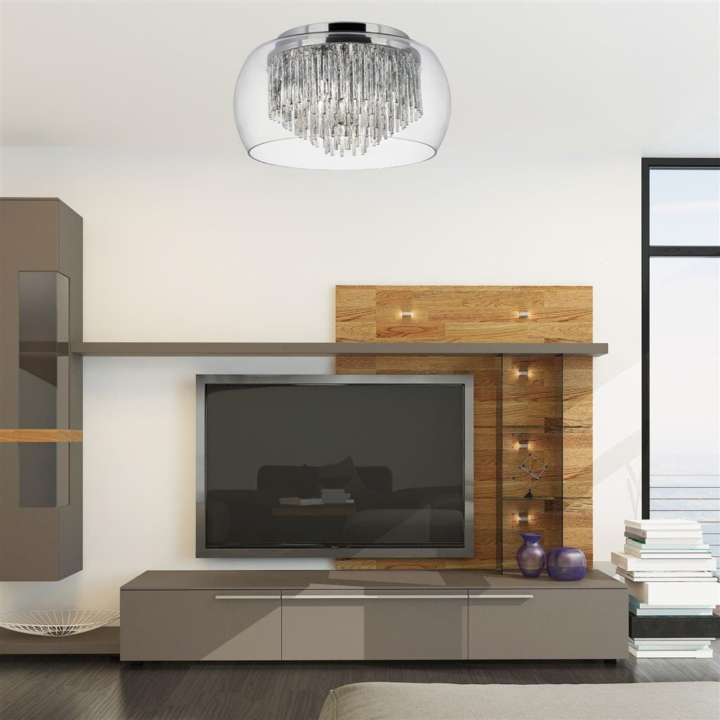 Lampa sufitowa Curva 4-punktowa w kolorze chromu z przezroczystym kloszem, ozdobiona wiszącymi kryształkami. Zainstalowana na suficie, w nowoczesnym wnętrzu z telewizorem i drewnianymi akcentami.