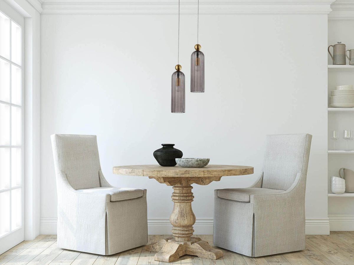 Lampa wisząca Piega 1-punktowa w kolorze patyny z dymionym kloszem, zawieszona nad okrągłym stołem z drewnianym blatem. W tle jasna ściana oraz dwa jasne krzesła obite tkaniną. Prosta aranżacja wnętrza.