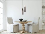 Lampa wisząca Piega 1-punktowa w kolorze patyny z dymionym kloszem, zawieszona nad okrągłym stołem z drewnianym blatem. W tle jasna ściana oraz dwa jasne krzesła obite tkaniną. Prosta aranżacja wnętrza.