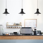 Czarna lampa wisząca Fisherman D32 z metalowym kloszem, zawieszona na cienkim przewodzie. Stylizowana na industrialną, umieszczona nad drewnianym blatem w jasnym wnętrzu kawiarni. W tle widoczne półki z napojami i akcesoriami.