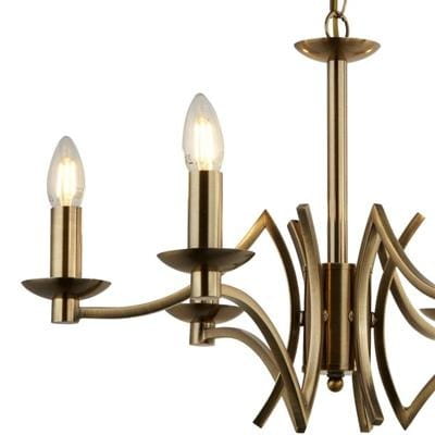 Lampa wisząca Ascot 6-punktowa w kolorze antycznego mosiądzu. Posiada sześć ramion w kształcie fal, z delikatnymi, przezroczystymi kloszami. Ujęcie z boku, pokazujące detale konstrukcji oraz elegancką formę.