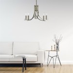 Lampa wisząca Ascona 5-punktowa w kolorze antycznego mosiądzu, z pięcioma ramionami, umieszczona nad białą sofą. Klosze w kształcie świeczników z przezroczystymi detalami, zawieszona na łańcuchu w minimalistycznym wnętrzu.