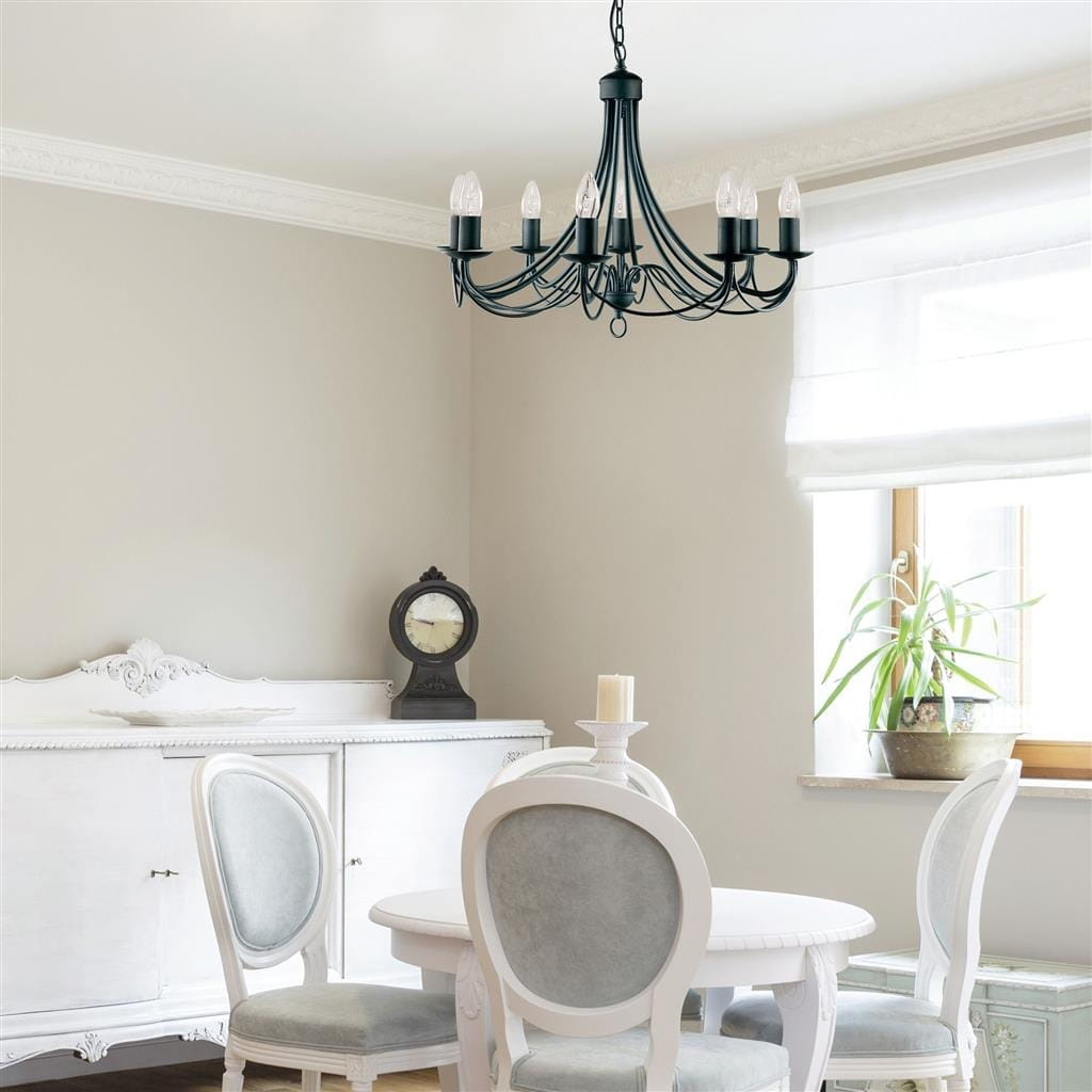 Lampa wisząca Maypole 8-punktowa w kolorze czarnym, z eleganckimi ramionami i miejscami na żarówki w kształcie świec. Zawieszona w jasnym wnętrzu, nad okrągłym stołem i białymi krzesłami, w otoczeniu zegara i roślin.