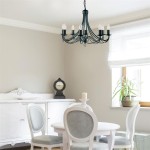 Lampa wisząca Maypole 8-punktowa w kolorze czarnym, z eleganckimi ramionami i miejscami na żarówki w kształcie świec. Zawieszona w jasnym wnętrzu, nad okrągłym stołem i białymi krzesłami, w otoczeniu zegara i roślin.