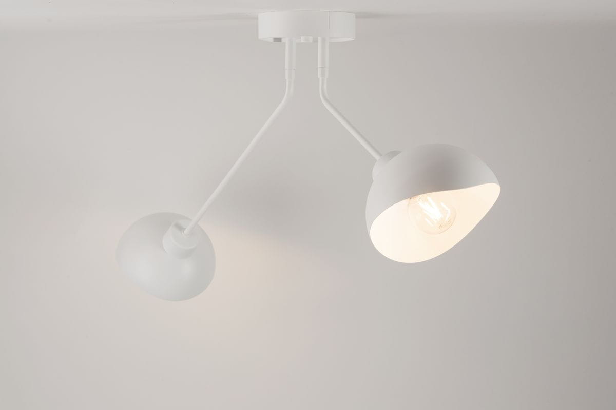 Lampa sufitowa Roy, dwupunktowa, w kolorze białym. Posiada dwa klosze w kształcie stożka, zamontowane na elastycznych ramionach. Ujęcie z dołu, na tle jasnej powierzchni, ukazujące źródła światła w kloszach.