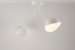 Lampa sufitowa Roy, dwupunktowa, w kolorze białym. Posiada dwa klosze w kształcie stożka, zamontowane na elastycznych ramionach. Ujęcie z dołu, na tle jasnej powierzchni, ukazujące źródła światła w kloszach.