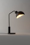 Lampa stołowa Roy w kolorze czarnym i białym, z zaokrąglonym kloszem i metalowym ramieniem. Ujęcie z boku, z widoczną podstawą i przewodem. Oświetlenie włączone, emitujące ciepłe światło. Prosta, nowoczesna forma idealna do biura lub salonu.