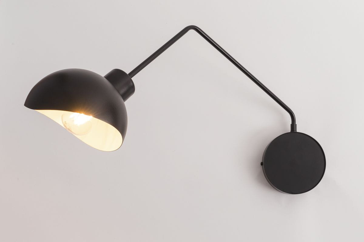 Kinkiet Roy 1-punktowy w kolorze czarnym i białym, z okrągłą podstawką. Lampa ma zaokrąglony klosz, który skierowany jest w dół, z metalowym wykończeniem. Ujęcie z boku, z widocznym lekko błyszczącym wnętrzem klosza.