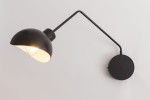 Kinkiet Roy 1-punktowy w kolorze czarnym i białym, z okrągłą podstawką. Lampa ma zaokrąglony klosz, który skierowany jest w dół, z metalowym wykończeniem. Ujęcie z boku, z widocznym lekko błyszczącym wnętrzem klosza.