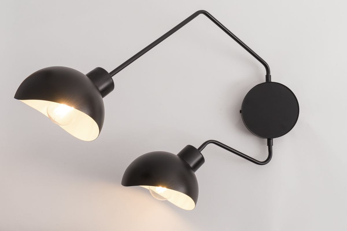 Kinkiet Roy z dwoma czarnymi kloszami w kształcie półkuli, z białym wnętrzem, zamontowany na okrągłej podstawie. Ujęcie z boku, pokazujące elastyczne ramiona. Produkt na jednolitym tle.