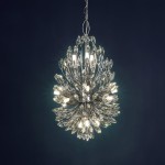Lampa wisząca Peacock 14-punktowa w chromowanej obudowie, z dekoracyjnymi kryształowymi elementami. Produkt zawieszony na łańcuchu, o kształcie przypominającym rozkwitający kwiat, emituje ciepłe światło z 14 żarówek. Tło ciemnoniebieskie.