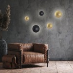 Kinkiet LED Platillo D21 12W CCT w kolorze czarnym, umieszczony na szarej ścianie, obok złotych i czarnych okrągłych elementów dekoracyjnych. W tle brązowa sofa z metalową ramą i torba.