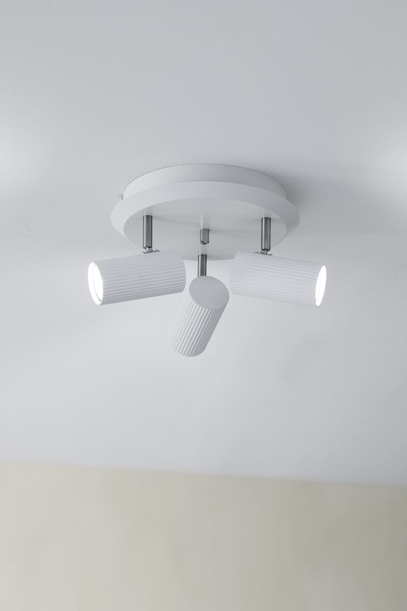 Lampa sufitowa Costilla 3-punktowa w kolorze białym. Posiada trzy cylindryczne klosze z wyraźnym żłobieniem, zamontowane na okrągłej podstawie. Ujęcie z dołu, ukazujące kąt ustawienia kloszy. Tło w jasnym kolorze, minimalistyczne.