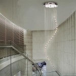 Lampa wisząca 5-punktowa w chromowanym wykończeniu, zawieszona na cienkich linkach. Kształt spiralny z kryształowymi kulkami, oświetlająca przestrzeń nad schodami w nowoczesnym wnętrzu. Surowe, jasne tło podkreśla elegancję lampy.