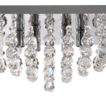 Lampa sufitowa 4-punktowa Hanna w kwadratowej obudowie chromowanej. Wyposażona w przezroczyste, wielokątne kryształy, które odbijają światło, tworząc efektowne refleksy. Ujęcie z bliska, ukazujące detale zawieszonego elementu.
