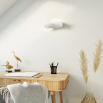 Mini kinkiet Sigma SL.0229 w kolorze białym, ceramiczny, zamontowany na ścianie. Produkt ma nowoczesny, falisty kształt. W tle widoczny drewniany stół z akcesoriami biurowymi i roślinami dekoracyjnymi.