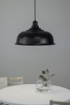 Czarna lampa wisząca Port D50 z metalowym kloszem o zaokrąglonym kształcie, zawieszona na cienkim przewodzie. Widoczna w aranżacji na białym stole z przezroczystą wazonem i gałązką rośliny w tle.