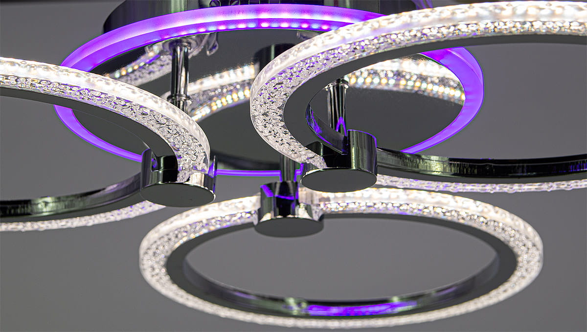 Lampa sufitowa Ring LED, 3-punktowa, chromowana, z trzema okrągłymi pierścieniami. Pierścienie zdobione kryształkami, emitujące białe i fioletowe światło. Ujęcie z bliska, ukazujące detale strukturalne i połysk powierzchni.