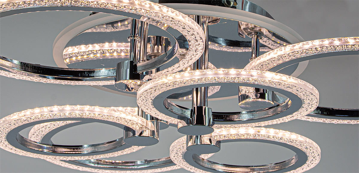 Lampa sufitowa LED Ring w chromowanej obudowie, składająca się z sześciu okrągłych punktów świetlnych. Okręgi zdobione kryształkami, z widocznym mocowaniem w centralnej części. Ujęcie z dołu, ukazujące detale konstrukcji oraz oświetlenia.