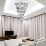 Lampa wisząca Sigma 9-punktowa w chromowanej obudowie, zawieszona w centralnej części pomieszczenia. Składa się z wielu szklanych elementów w kształcie kryształów, które odbijają światło, w eleganckim wnętrzu z beżowymi zasłonami i drewnianym meblem.
