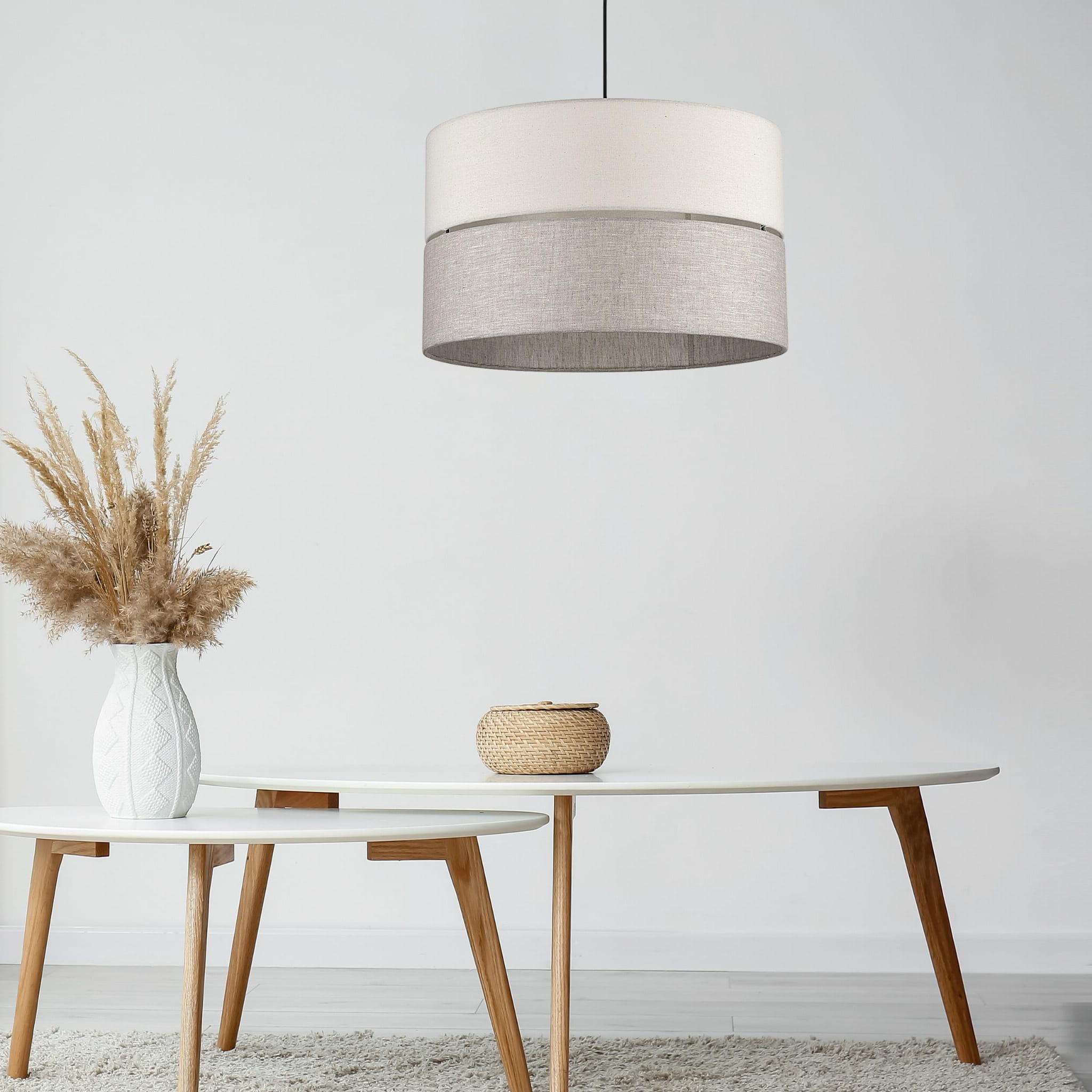 Lampa wisząca Eco D38 w kształcie cylindrycznym, z materiału w kolorze jasnym i szarym, zawieszona nad białym stołem. W tle widoczna dekoracja w wazonie oraz koszyk, na stonowanym tle.
