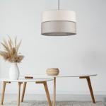 Lampa wisząca Eco D38 w kształcie cylindrycznym, z materiału w kolorze jasnym i szarym, zawieszona nad białym stołem. W tle widoczna dekoracja w wazonie oraz koszyk, na stonowanym tle.
