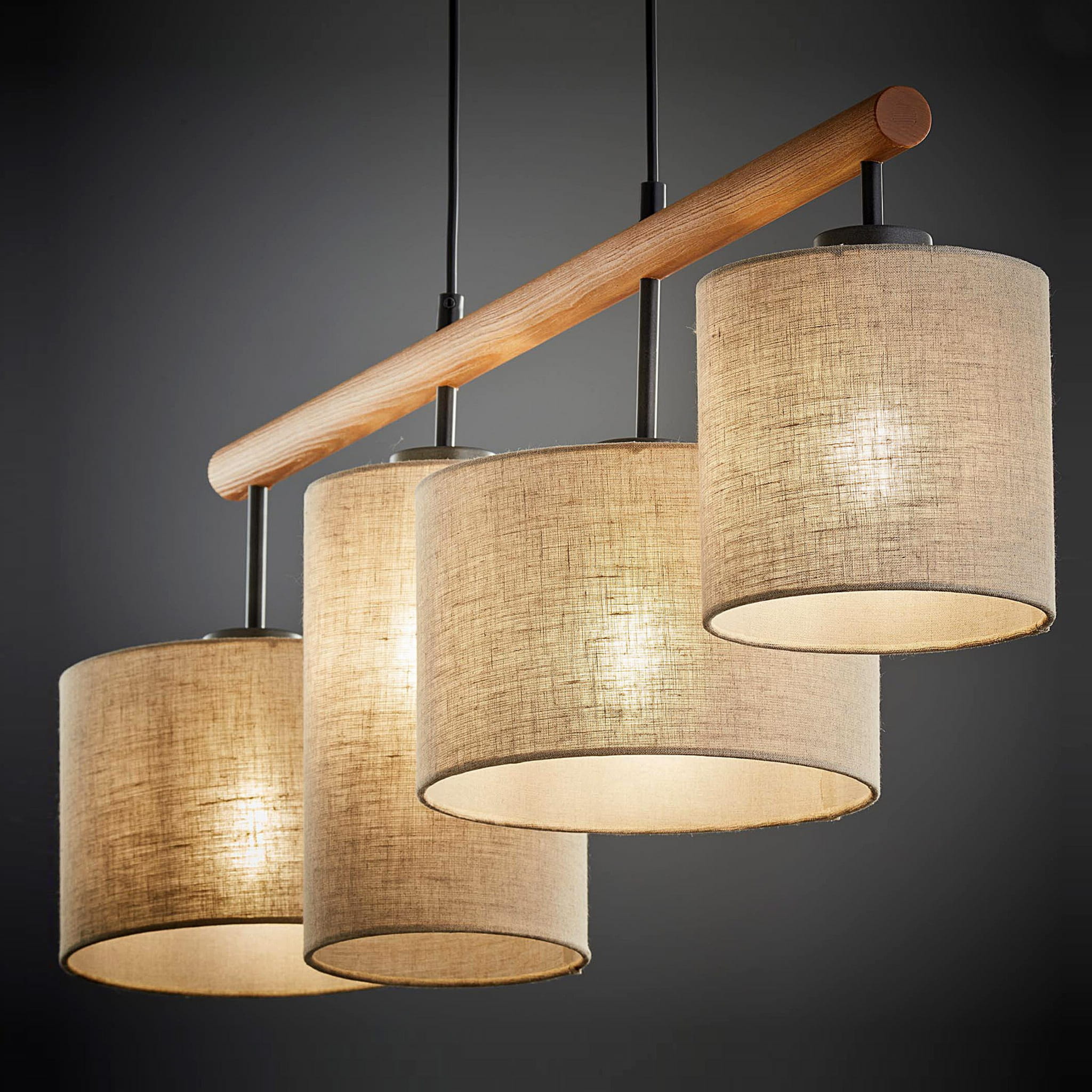 Lampa wisząca Deva Nature 4-punktowa 6108 z czterema okrągłymi abażurami w jasnym kolorze, wykonanymi z materiału tekstylnego. Konstrukcja z drewnianym uchwytem i metalowymi elementami. Ujęcie z przodu na ciemnym tle.