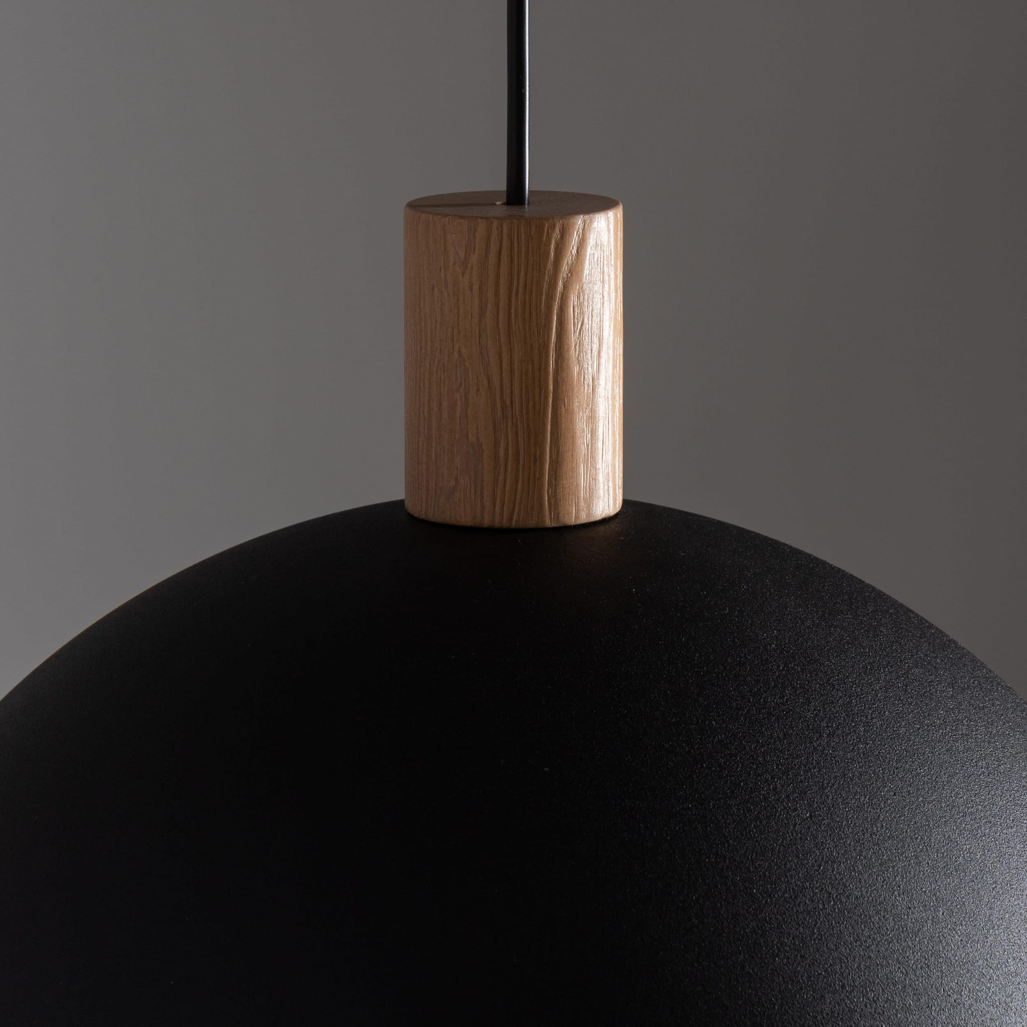 Czarna lampa wisząca Oslo z 1 punktem świetlnym, o okrągłej, matowej czaszy i drewnianym detalem na górze. Lampa zawieszona na cienkim przewodzie, ukazująca minimalistyczny design i elegancki styl.