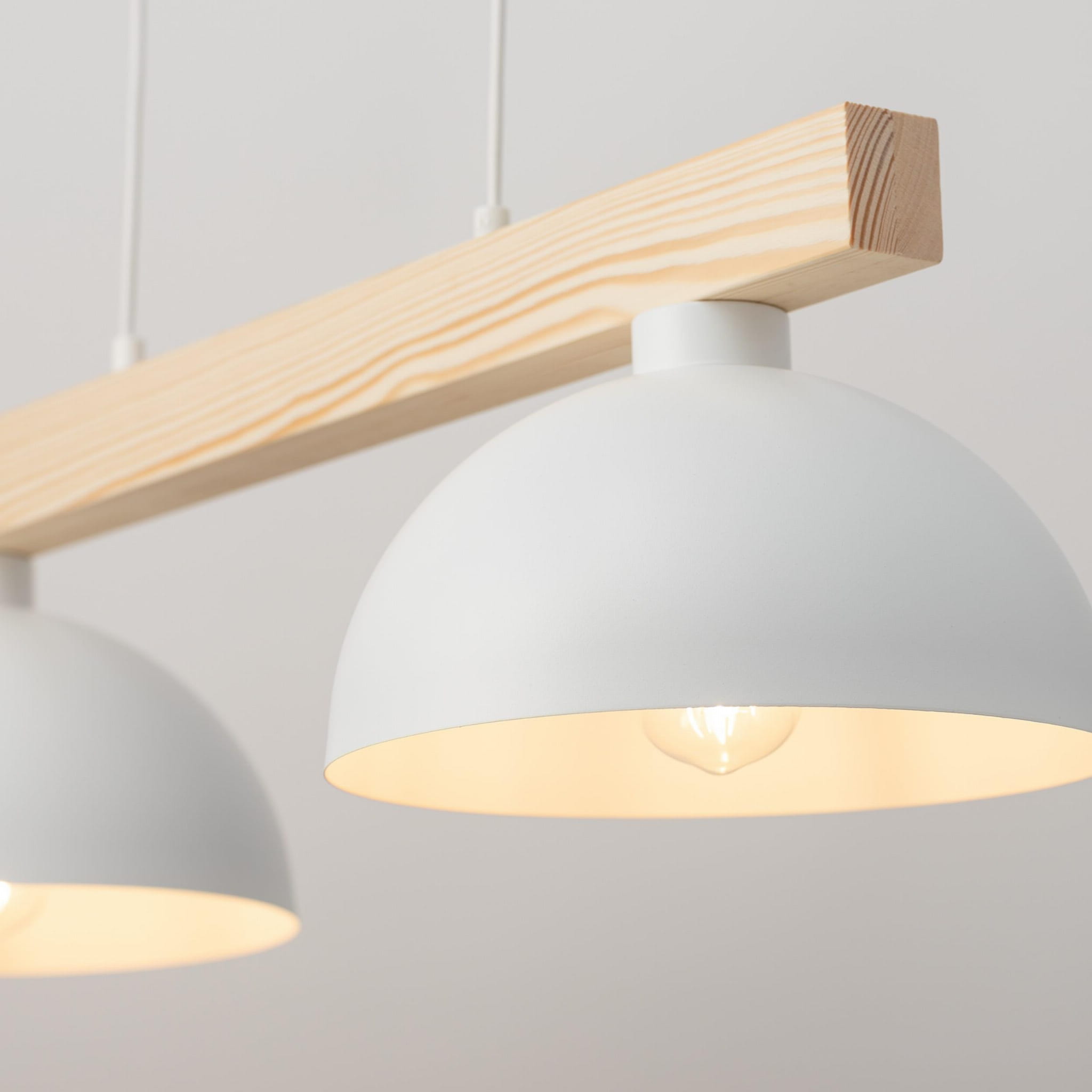 Lampa wisząca Oslo 2-punktowa, biała, z drewnianym zawieszeniem. Dwa okrągłe klosze w kolorze białym, emitujące ciepłe światło. Kąt ujęcia zbliżenie na klosze i detal konstrukcji. Tło jasne, minimalistyczne.