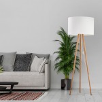 Lampa podłogowa Tokyo z białym kloszem na drewnianych nogach z sosny, stojąca w jasnym wnętrzu obok szarej kanapy i rośliny w doniczce. Klosz w kształcie walca, z widocznym włącznikiem na przewodzie.