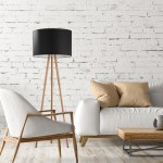 Lampa podłogowa Tokyo 1-punktowa w kolorze czarnym z abażurem na trójnogu z sosny. Ustawiona obok jasnej, komfortowej sofy z beżowymi poduszkami, na tle białej ceglanej ściany.