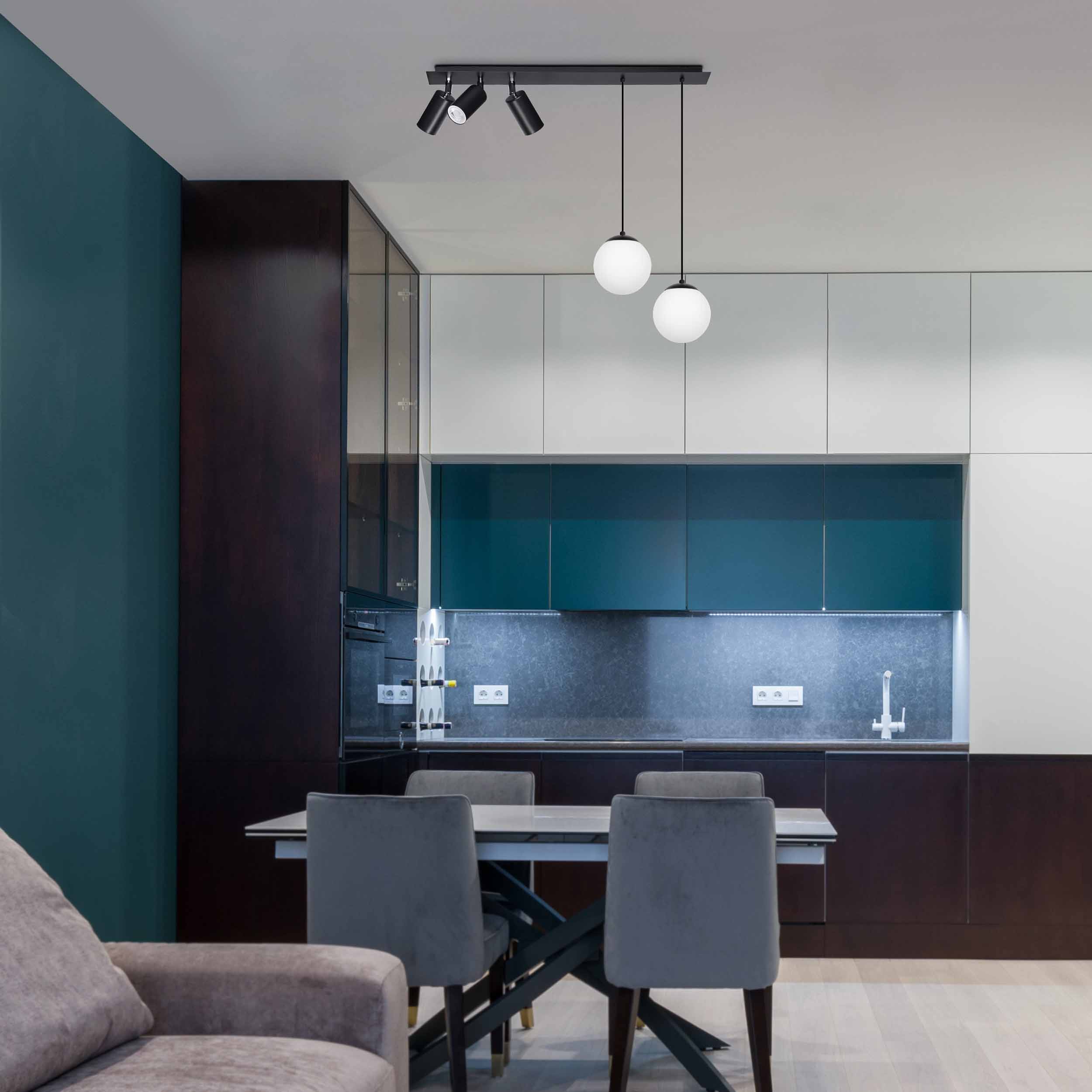 Lampa wisząca Albio 5-punktowa czarna K-4138 z trzema okrągłymi, białymi kloszami i dwoma punktami świetlnymi w formie czarnych reflektorów. Zawieszona na prostokątnej podstawie, umieszczona w nowoczesnej kuchni z ciemnymi meblami.