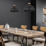 Czarna lampa wisząca Cap 1-punktowa z drewnianym detalem, zawieszona nad drewnianym stołem w nowoczesnej jadalni. W tle ciemna ściana oraz krzesła z naturalnego drewna.