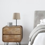 Lampa stołowa Chicago 1-punktowa, czarna podstawa metalowa, abażur z lnu w kolorze beżowym. Ustawiona na drewnianej szafce nocnej obok szarego zegara. Tło jasne, minimalistyczne wnętrze sypialni.