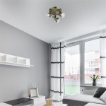 Lampa sufitowa (spot) Focus, 3-punktowa, w kolorze antycznego mosiądzu. Ułożona w sufit, z trzema reflektorami skierowanymi w różnych kierunkach, w nowoczesnym wnętrzu z szarymi ścianami i dużymi oknami.