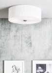 Lampa sufitowa Jackie D45 w kolorze białym, okrągła, z plisowanym kloszem, zamontowana na suficie. Widoczne detale to metalowy element mocujący. Tło w odcieniach szarości z obrazami na ścianie.