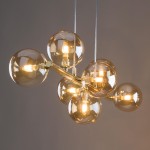 Złota lampa wisząca Estera z siedmioma przezroczystymi kulami. Kule umieszczone na metalowej ramie, emitujące ciepłe światło. Lampa zawieszona na cienkich, przezroczystych linkach, doskonale nadaje się do nowoczesnych wnętrz.