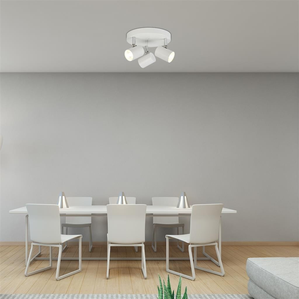Trzypunktowa lampa sufitowa Rollo LED w kolorze białym, zamontowana na okrągłej podstawie. Reflektory w kształcie cylindrów skierowane w różne strony, w jasnym, minimalistycznym wnętrzu z białym stołem i krzesłami.