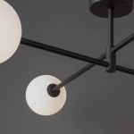 Czarna lampa sufitowa Sarius 4-punktowa z metalowymi ramionami. Dwa białe, okrągłe klosze z matowego szkła, umieszczone na czarnych prętach. Lampa montowana sufitowo, widok z dołu, na tle ciemnej ściany.